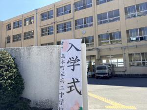 第二中学校の校門前の写真。学校の校舎を背景に入学式の立て看板が写った写真